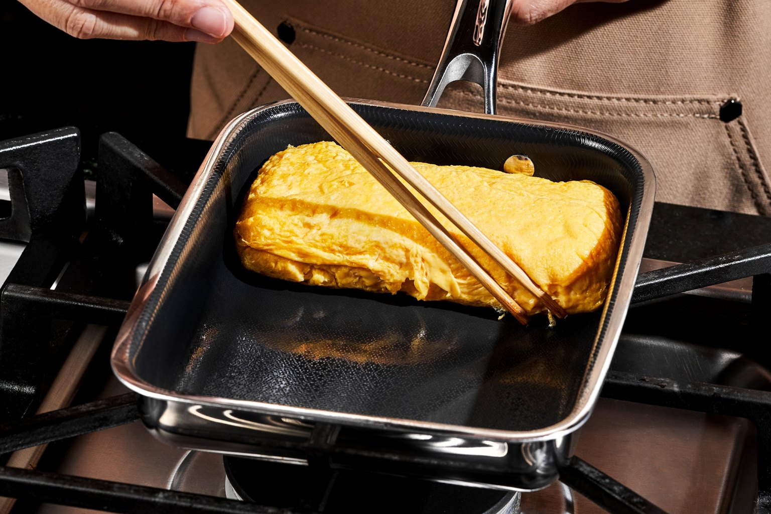 HexClad's Japanese egg pan on a gas hob, with a rolled omelette being lifted by chopsticks